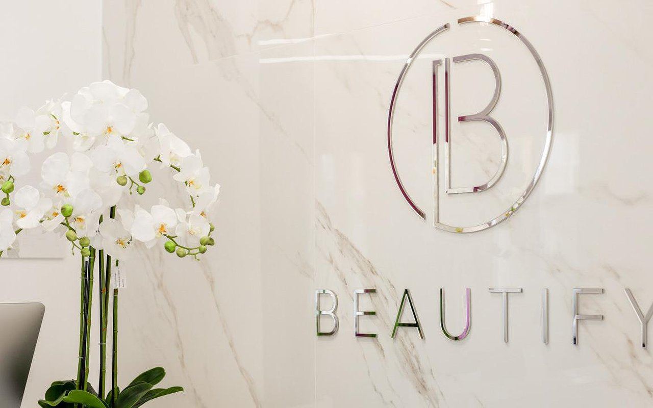 Logo Beautify in acciaio sulla parete in marmo con orchidee bianche