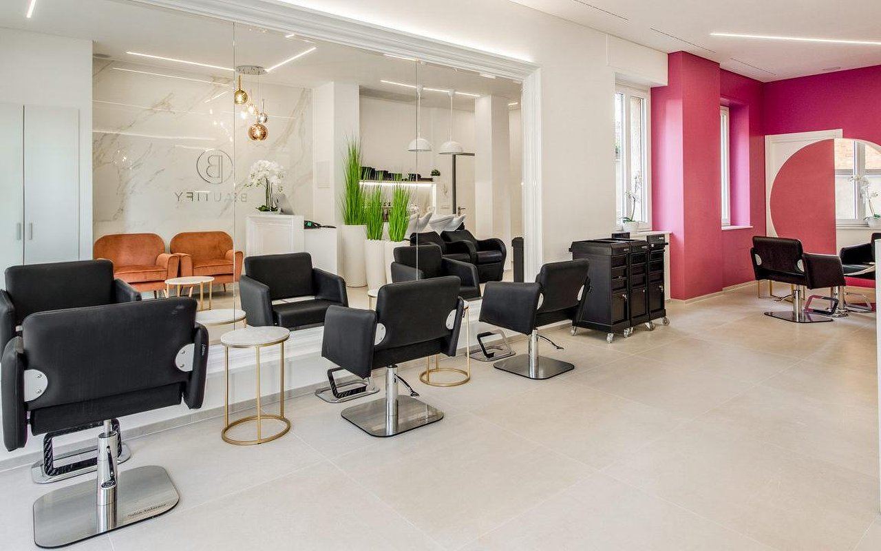 Il salone Beautify: postazioni nere, pavimento chiaro, parete fucsia e logo sulla parete in marmo